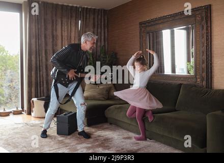 Father rock guitarist having fun and and dancing with his little daughter at home. Stock Photo