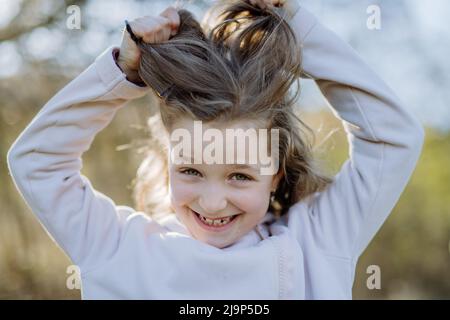 Funny portrait of pretty child girl standing in summer park looking in camera smiling happily. Stock Photo