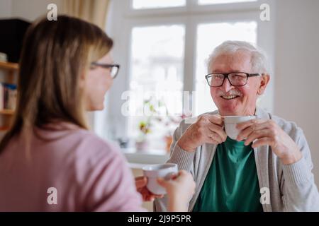 Adult daughter visiting her senior father at home and having coffee together, talking. Stock Photo