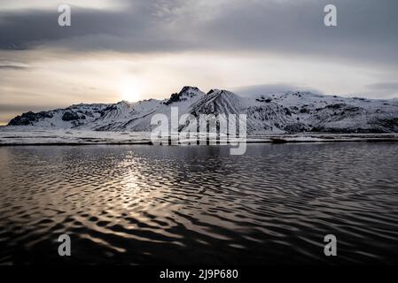 Beautiful snow-covered winter landscape at Öræfi / Öræfasveit, with the evening sun reflected in the rippled water of a lake, near Skaftafell, Iceland Stock Photo