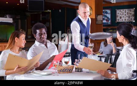 Polite waiter bringing ordered drinks to restaurant guests Stock Photo