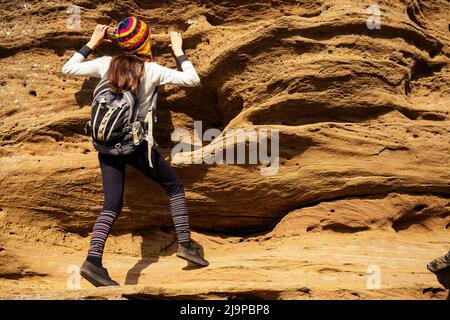 Beautiful slim and sporty young tourist woman in a funny hat from Nepal wool yak climbing big rock climbs on boulders canyon stones Stock Photo