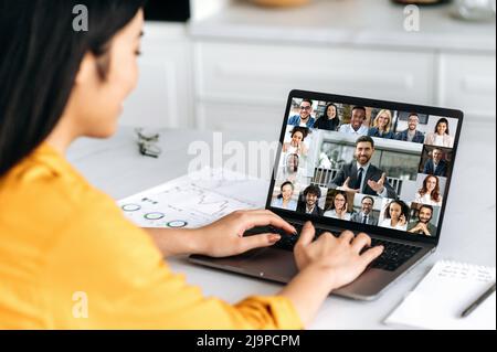 Virtual meeting, brainstorm of colleagues, online conversation. Over shoulder view of a girl to a laptop screen, talking on video call with multiracial business group, discussing the project, start-up Stock Photo