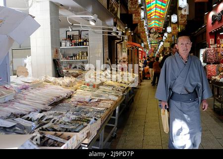A Japanese man in a traditional yukata walks past a dried goods store at the Nishiki Markets in Kyoto, Japan Stock Photo