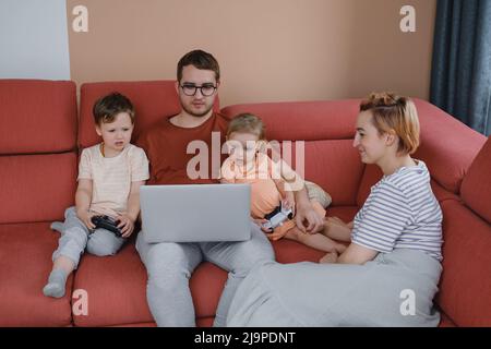 Big happy family watching movies playing games on laptop. Mother father kids spending time with gadgets on sofa Children with parents looking on Stock Photo