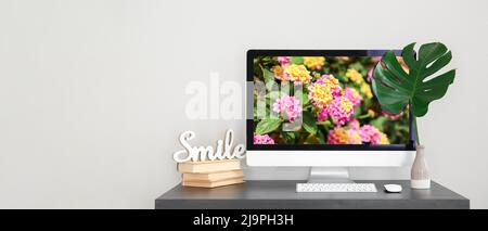 Workplace with computer, tropical leaf in vase and books on light background with space for text Stock Photo
