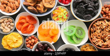 Bowls with different dried fruits and nuts on dark wooden background, top view Stock Photo