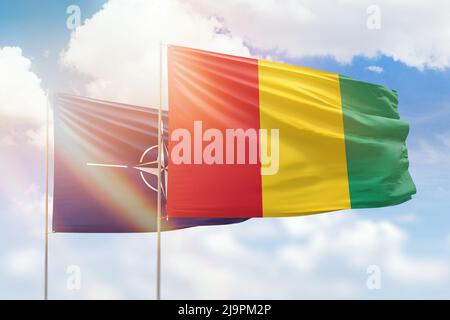 Sunny blue sky and flags of guinea and nato Stock Photo