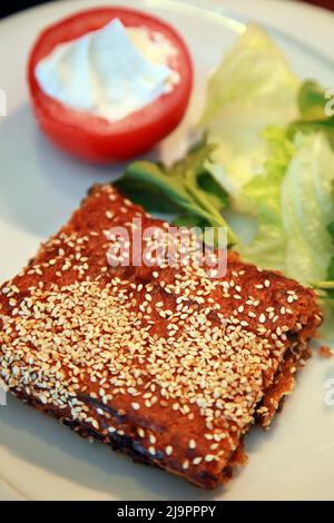 Cheese pastry (Turkish: Peynirli Börek) with sesame and tomato and lettuce on the dinner plate. Stock Photo