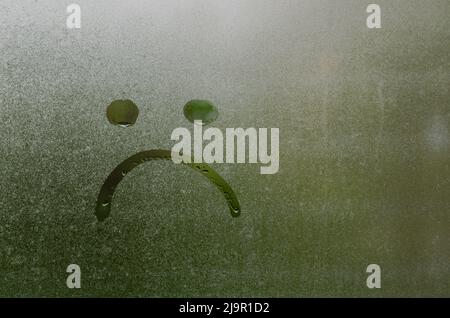 Face expession as boring and sad painted on window which fogged up after rain with blurred green color background. Stock Photo