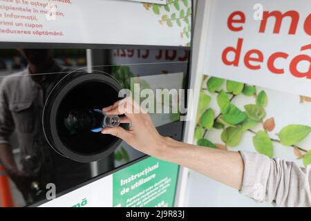 Bucharest, Romania - May 25, 2022: Details with the hands of a man introducing glass bottles in a recycling equipment. Stock Photo