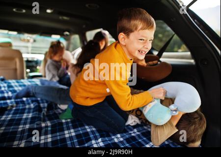 Two brothers fighting pillows at vehicle interior. Children in trunk. Traveling by car in the mountains, atmosphere concept. Stock Photo