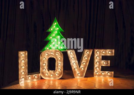 Metal letters with electric lights in the word LOVE and a glowing Christmas tree. Stock Photo