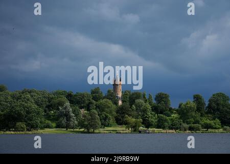24 May 2022, Brandenburg, Potsdam: Dark clouds pass over Babelsberg Park and the Flatow Tower, which are located at the Tiefen See lake. The weather in Berlin and Brandenburg remains changeable. According to the forecast of the German Weather Service (DWD), Wednesday will start with a mix of sun and clouds and mostly dry. Around noon and in the afternoon, however, it may rain and occasionally thunderstorm briefly. On Ascension Day, according to the forecast, a mix of sun and clouds is to be expected. With temperatures between 20 and 22 degrees, the holiday is ideal for outdoor excursions. Phot Stock Photo