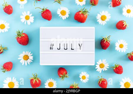 Summer month July text on light box and strawberry, chamomile flowers on blue background. Creative concept Hello July. Top view, Flat lay, greeting ca Stock Photo