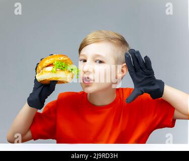 The boy is holding a burger in front of him. He has black gloves on his hands. Stock Photo