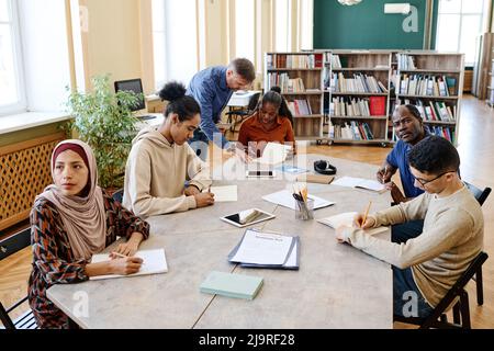 High angle view shot of mature teacher working with multi-ethnic group of immigrant students in library Stock Photo
