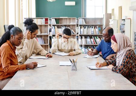 Group of ethnically diverse immigrants learning English language at school sitting in library doing grammar test Stock Photo