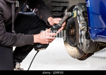 Car detailing - Hand with orbital polisher in auto repair shop, polishing modern car brakes Stock Photo