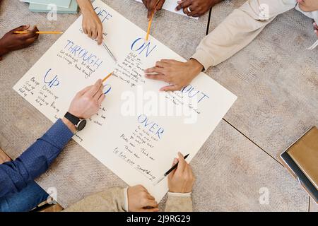 High angle view of unrecognizable group of students learning English phrasal verbs using handmade poster Stock Photo