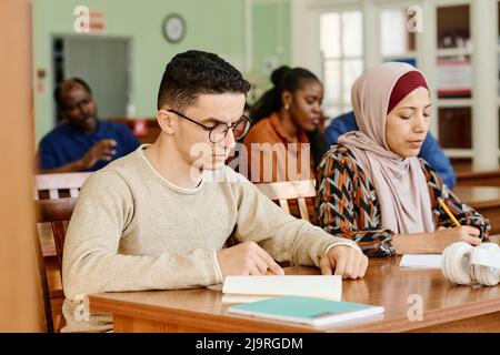 Group of immigrant students in international class sitting at desk reading and making notes during lesson Stock Photo