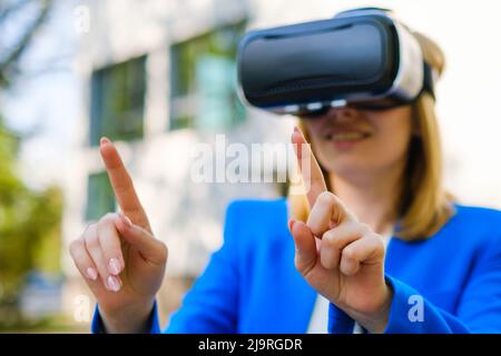 Business woman using VR goggles, moving her head touching the simulation screen in the park.  Stock Photo