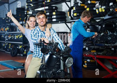 couple sitting on new motorbike in workshop. Stock Photo