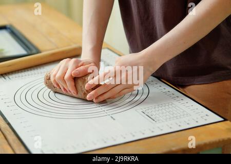 Close-up on female hands that knead the dough for gingerbread cookies on a baking mat. Stock Photo