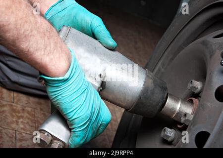 Mechanic changing wheel on car with impact wrench. mechanic man with electric screwdriver. Stock Photo