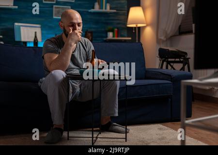 Male person switching channels with TV remote control, changing programs to find movie. Young man watching film or show on television screen, doing leisure activity on couch for entertainment. Stock Photo