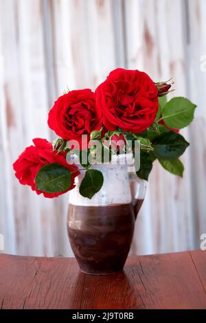 Red roses in an earthenware vase on a wooden table. Stock Photo