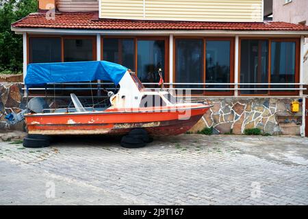 Abandoned wooden boat ashore in front of a house. Stock Photo