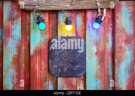 Blank or empty metal plaque illuminated with colorful light bulbs on multicolored steel wall plate. Stock Photo
