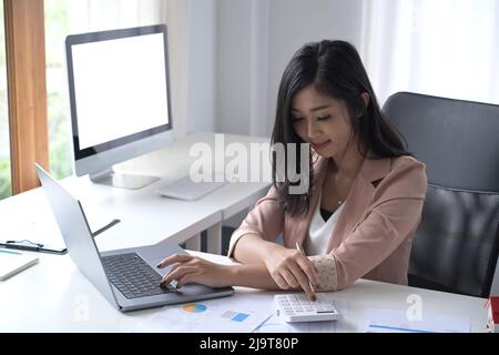 Thoughtful businesswoman using calculator and preparing annual financial report at workplace. Stock Photo
