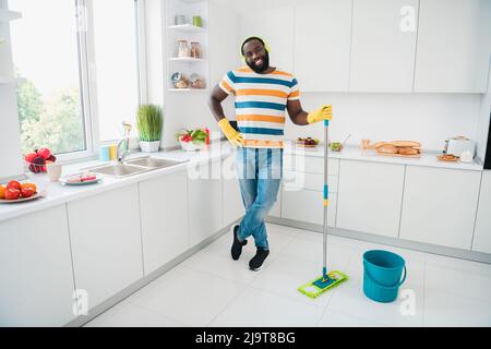 Full body portrait of cheerful funny person hold mop enjoy wireless mo3 sound standing kitchen room house indoors Stock Photo