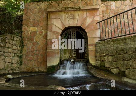 Hot water source in Niska Banja, Serbia on spring day. Water springs from the fenced tunnel of the fountain in the forest. Long exposition of water Stock Photo