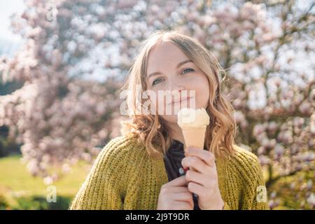 Beautiful young blonde hair woman with vanilla ice cream in a waffle cone looks at the camera and smiles Stock Photo