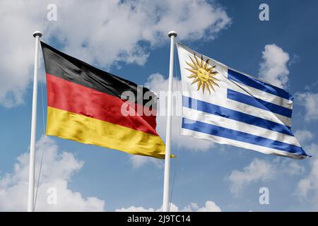 Germany and Uruguay two flags on flagpoles and blue cloudy sky background Stock Photo