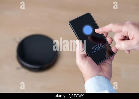 A man controls his cleaning robot via his cell phone. New technologies in the home. Connecting devices via wifi and bluetooth Stock Photo