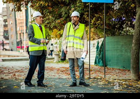 Two construction workers are standing while talking to each other about the plans Stock Photo
