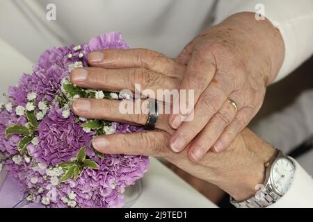 Elderly Couple on their wedding day. 80 year old couple holding hands and showing their wedding rings and bouquet Stock Photo