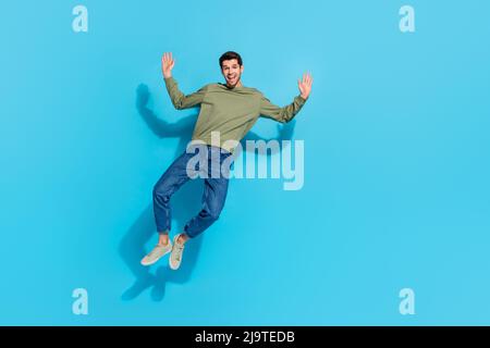 Full size photo of impressed young brunet guy jump wear shirt jeans sneakers isolated on blue background Stock Photo