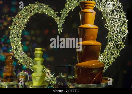 display of dark and white chocolate fountains on a background decorated with a heart and light. Stock Photo
