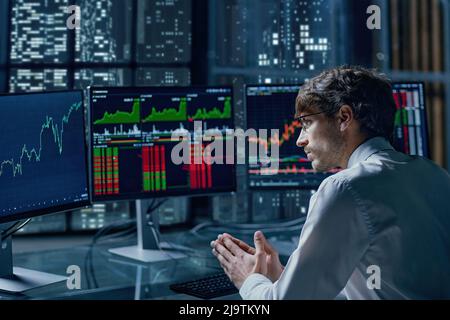 thoughtful young investor looking at his computer monitors . Stock Photo