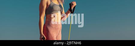 Strong woman in sportswear exercising on sports site, using fitness resistance bands Stock Photo