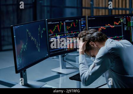 frustrated investor sitting in front of the working monitors of his computers. Stock Photo