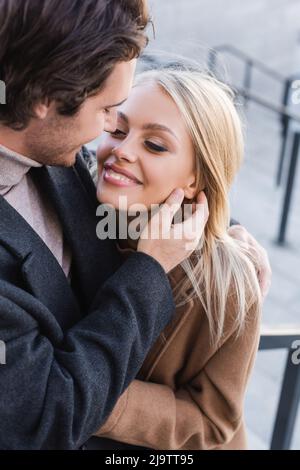 young blonde woman smiling near man in coat outdoors Stock Photo