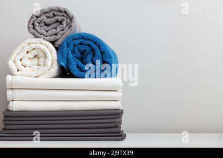 Stack of bed linen, sheets, rolled up terry towels on the table Stock Photo