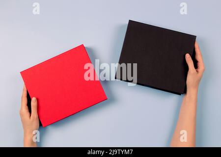 Woman hands holding red and black elegant luxury boxes. Mockup present gift boxes on light blue background. Top view Stock Photo