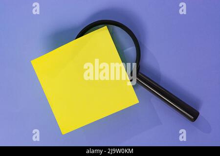 Adhesive Note With Magnifying Glass Against Purple background. Directly Above. Flat Lay. Copy Space. Business Concept. Stock Photo